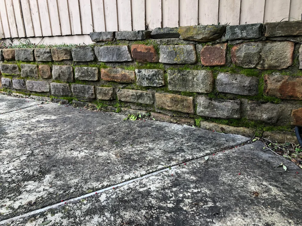 Moss-covered stone retaining wall before pressure washing